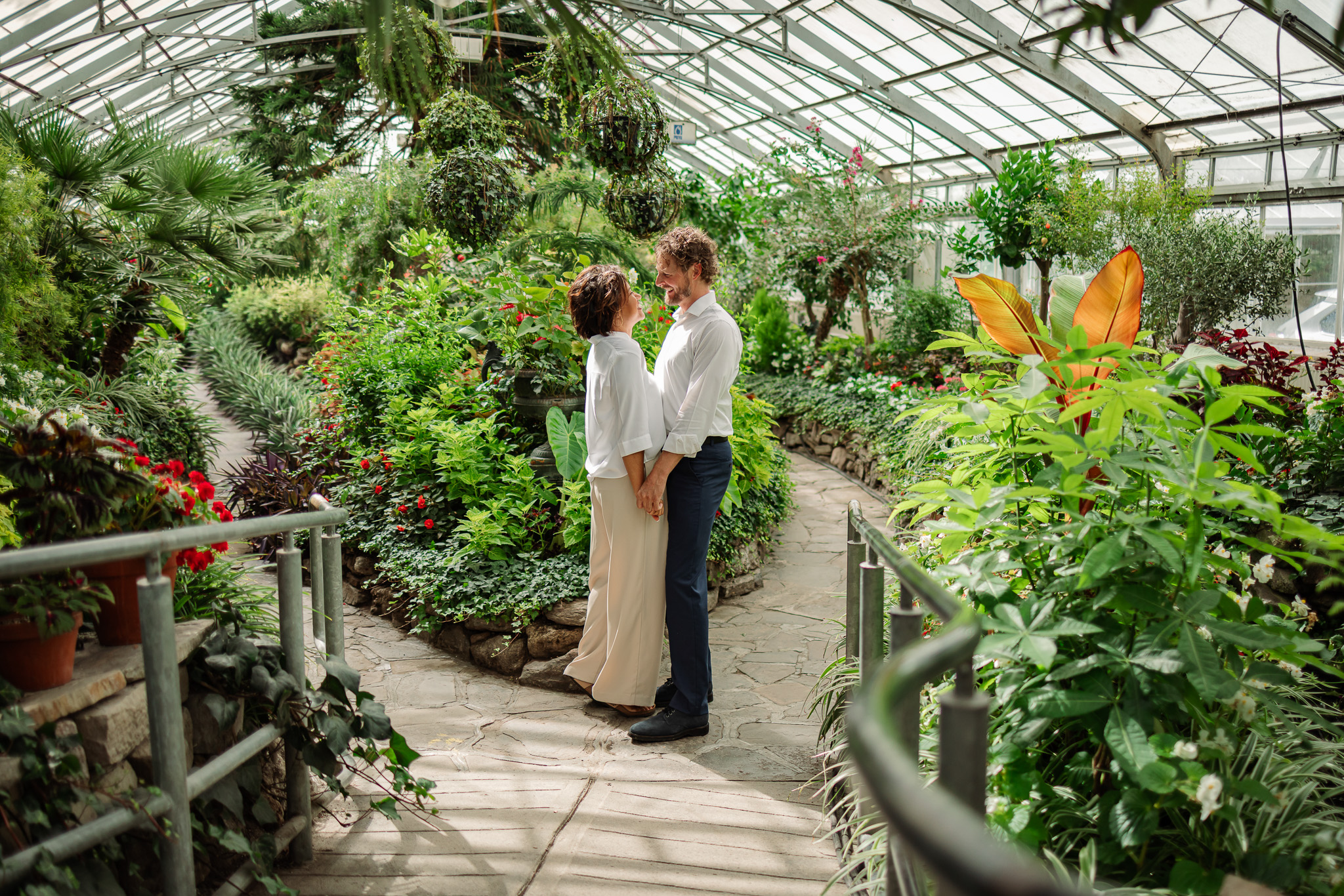 Engaged couple embracing near tropical plants and flowers at Allan Gardens Conservatory engagement photos in downtown Toronto.