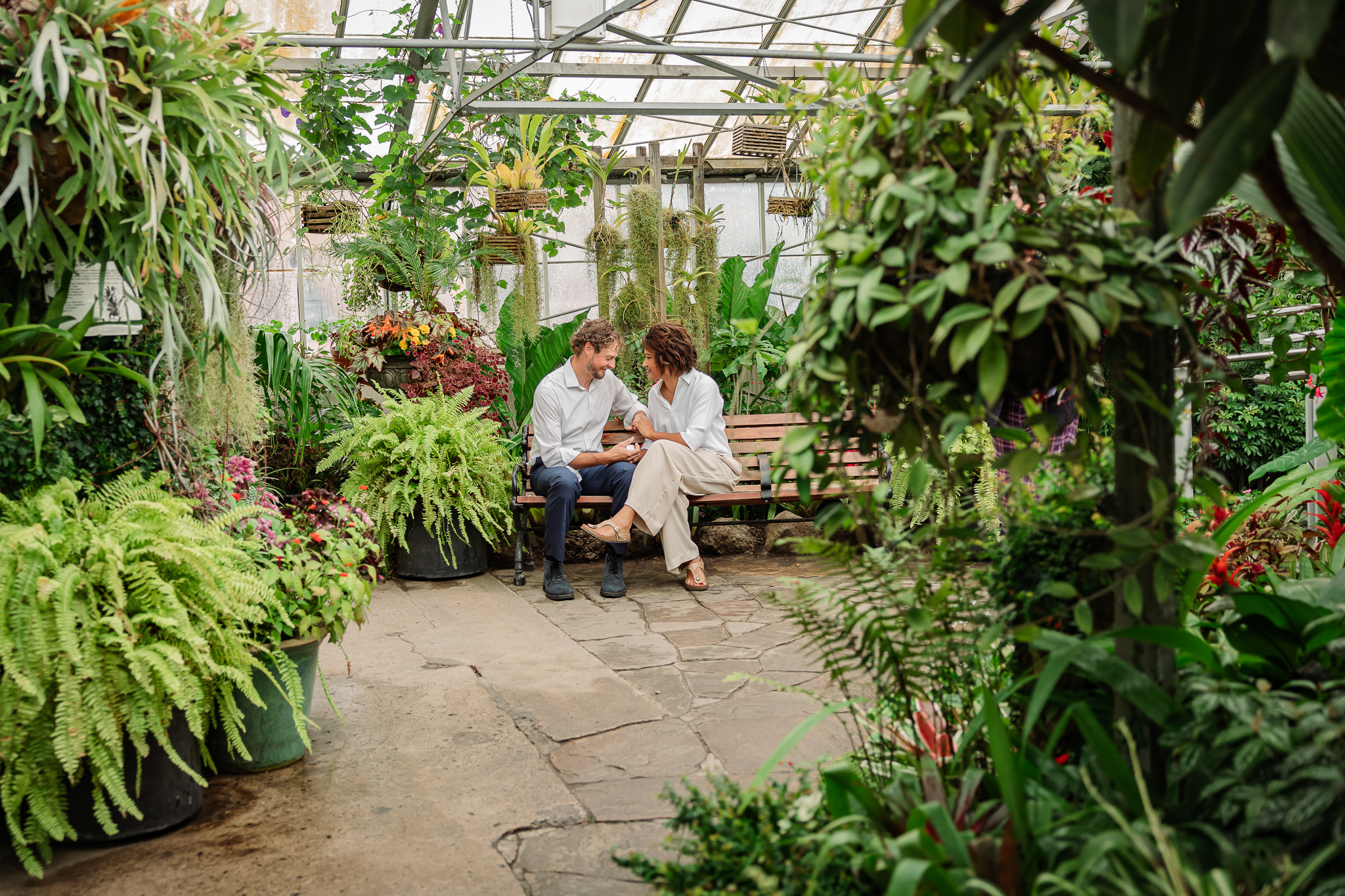 Indoor engagement photos Toronto at Allan Gardens with couple sitting on garden bench surrounded by tropical plants.