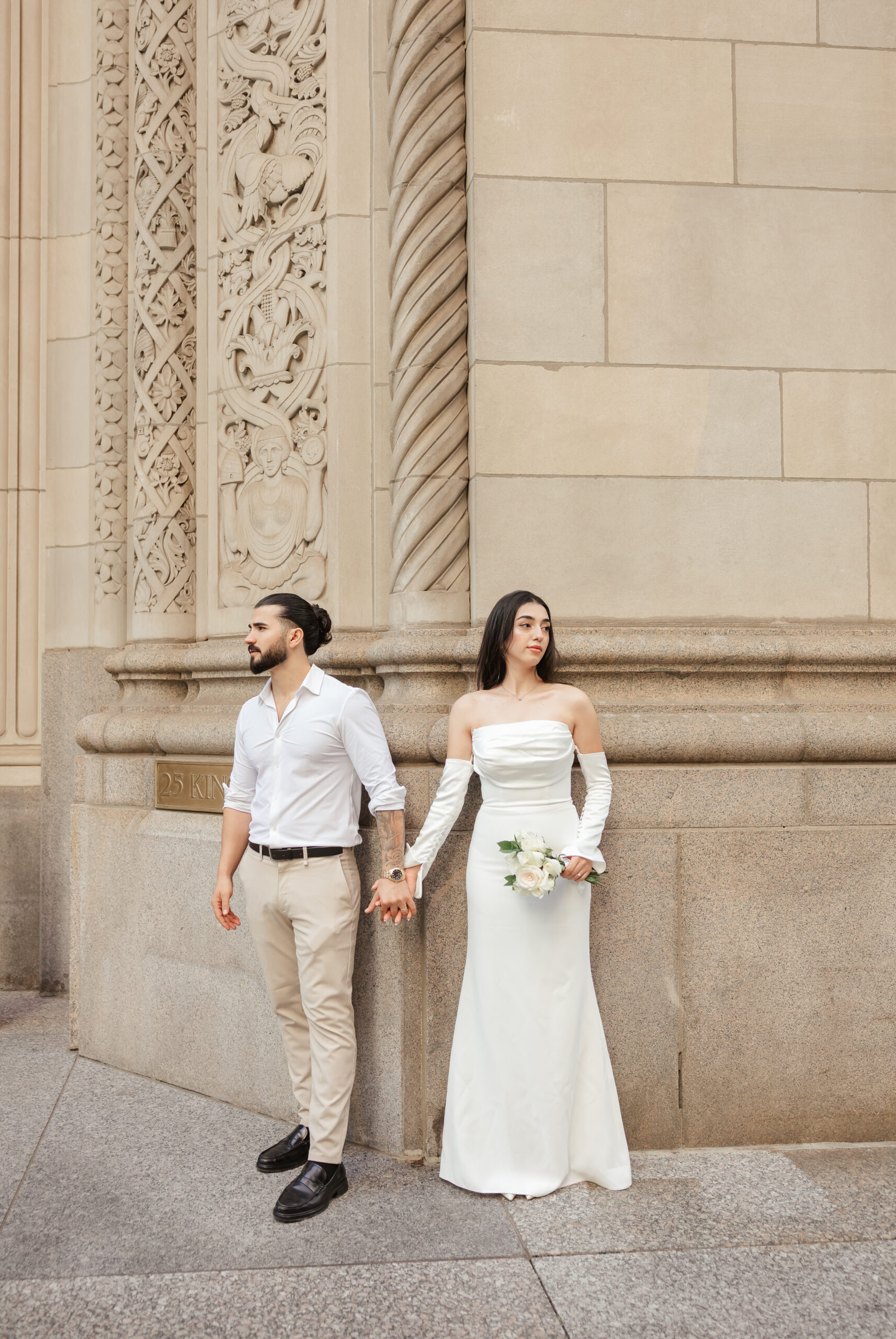 Elegant downtown Toronto elopement photo of a couple holding hands against stone architecture, captured by Spark Maple Media.